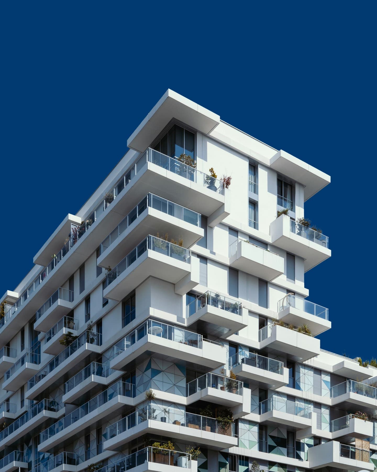 A white residential tower with stepped balconies against a deep blue sky
